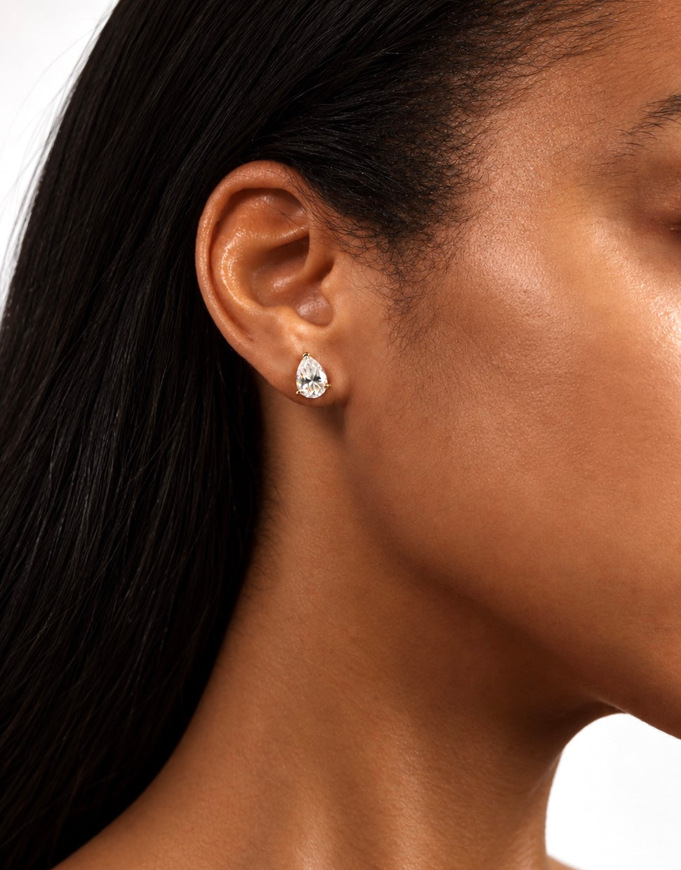 A close-up side profile of a woman wearing a small 2 carat teardrop-shaped pearcut clear gemstone stud earring in a yellow gold -toned setting.